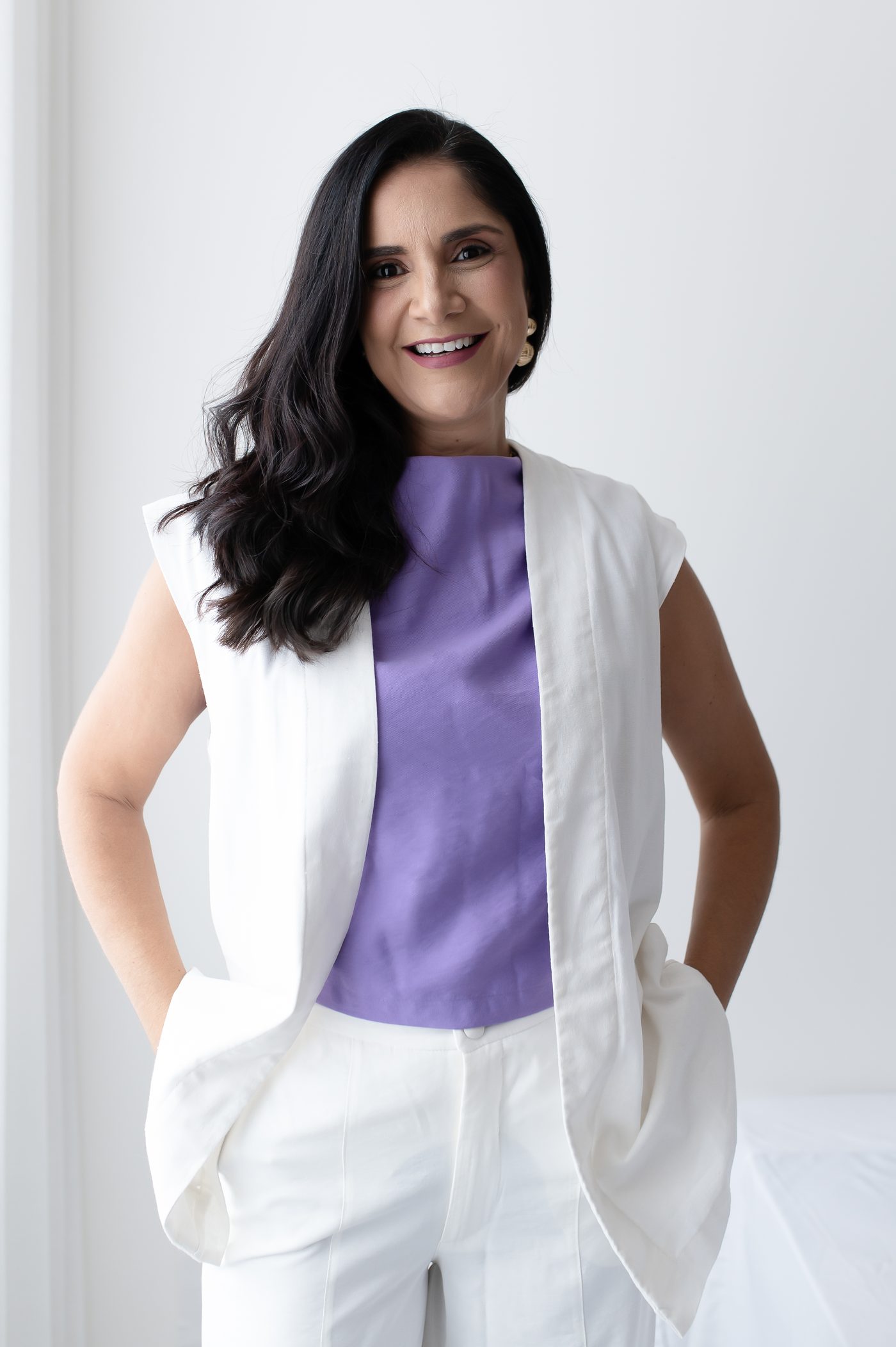 Fabíola Lacerda sorrindo, de braços cruzados, vestindo colete branco sobre blusa lilás